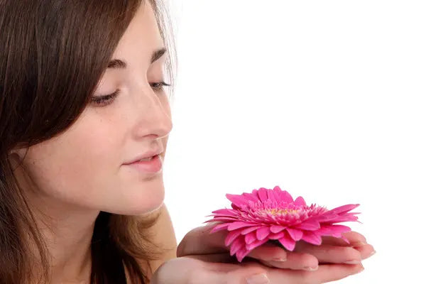 Young woman gently holding a pink flower close to her face
