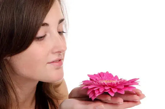 Young woman gently holding a pink flower close to her face