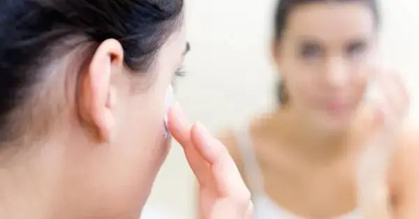Person applying cream to their face while looking in a mirror